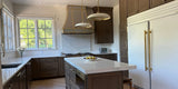 Completed dark wood kitchen with a custom brass-trimmed range hood built directly to the ceiling